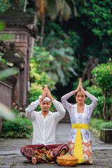 balinese hindu couple put their hand on top of their head while doing the prayer at pura in the morning