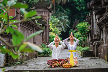 balinese couple do the prayer to god in the morning. hindu people make an offering to their god using canang