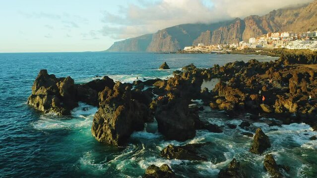 Touristic spot. Aerial sunset light on ocean waves and rocks. Tenerife, Canary Island, town Puerto de Santiago, Charco el Diablo or natural pool of Devil. Lava flows, volcanic bizzare stone beach