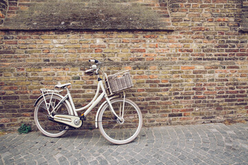 White vintage bicycle standing in front of brick wall in the city of Bruges, Belgium