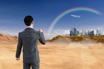 一人のビジネスマンが大自然にある虹のかかるビジネス街を見つけ、希望を胸にやる気でガッツポーズをする