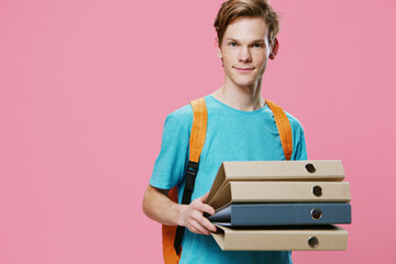 a handsome guy with an orange backpack on his back holds empty note folders in his hands, smiling pleasantly at the camera. Horizontal photo on a pink background with empty space for advertising text