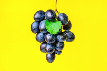 candied fruit black grapes with green leaves close-up yellow background