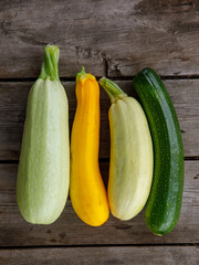 fresh mixed yellow, white, stripped and green zucchini's on a wooden background. Top view flat lay, close up. Vertical