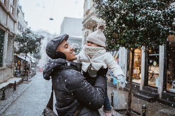 portrait of father carrying his daughter during snow fall in the city