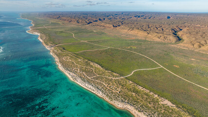 Areal view of the coastline in Cape Range National Park. The turquoise waters meeting the dry yet green bushland next to the rugged ridges of the range.