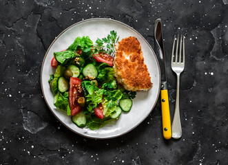 Fresh vegetable salad and fried halumi in bread crumbs - a delicious vegetarian lunch on a dark background, top view
