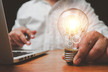 The hand of a man with a light bulb And there is a gear icon in it And he is using a notebook computer. idea of creativity and inspiration concept. The idea of ​​inspiration from online technology.