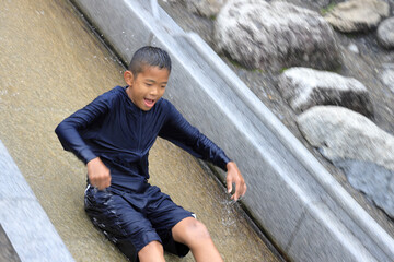 川のウォータースライダーで遊ぶ男子中学生 (12歳)