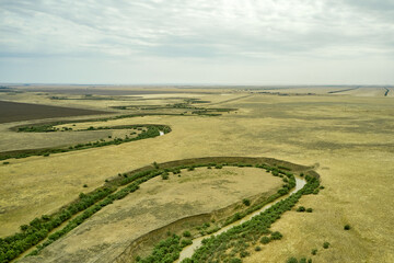 a winding muddy river with overgrown green banks in a sun-scorched steppe rural landscape