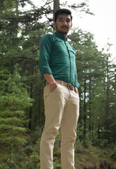 Guy wearing formal clothes outdoor in cedar forest looking down at camera, hand in pocket