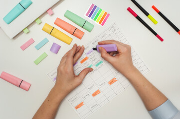 Planning the school year. Drawing up a student schedule. The girl makes edits with a purple marker in the planner on the white table. Multicolored markers and stickers on a white table.