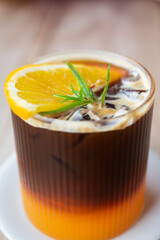 Top view Closeup of iced black coffee mixed with orange juice in a glass with slices of orange, rosemary leaves.