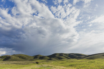 Fototapeta na wymiar Green grassy plain and hills with cloudy sky