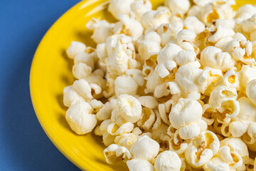 Popcorn on a yellow plate on blue background, Food or snack, Health or salt