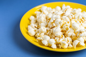 Popcorn on a yellow plate on blue background, Food or snack, Health or salt