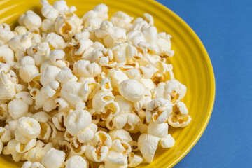 Popcorn on a yellow plate on blue background, Food or snack, Health or salt