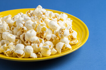 Popcorn on a yellow plate on blue background, Food or snack, Health or salt