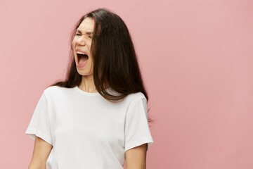 emotional, angry, woman with dark hair color stands in a white t-shirt on a pink background and...