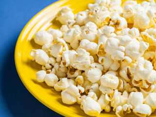 Popcorn on a yellow plate on blue background, Food or snack, Health or salt