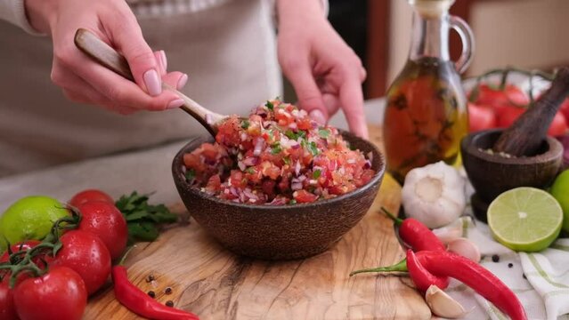 woman mixing salsa dip sauce ingredients in wooden bowl