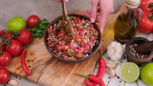 woman mixing salsa dip sauce ingredients in wooden bowl