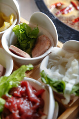 A view of several ingredient selections to add to a hot pot meal, featuring slices of spiced ham.