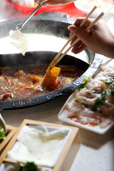 A view hand dipping raw meat slices into the broth bowl, seen with of all the elements of a hot pot restaurant meal.