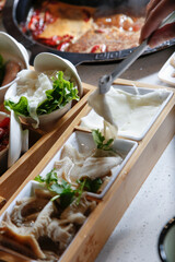 A view of a hand and tongs grabbing a slice of raw tripe, part of a hot pot meal.