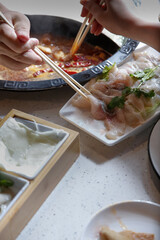 A view hand dipping raw meat slices into the broth bowl, seen with of all the elements of a hot pot restaurant meal.