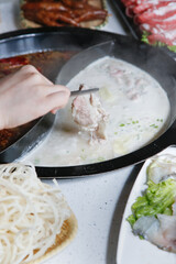 A view hand dipping raw meat slices into the broth bowl, seen with of all the elements of a hot pot restaurant meal.