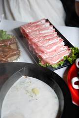 A view of all the elements of a hot pot meal, featuring a plate of raw beef slices.
