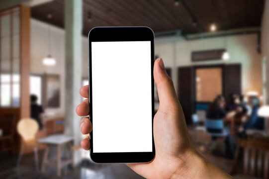 Mockup image of hand holding white mobile phone with blank white screen in cafe.