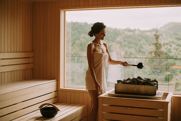 Young woman pouring water onto hot stone in the sauna