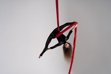 Flexible female circus Artist perform on red aerial silk on white background