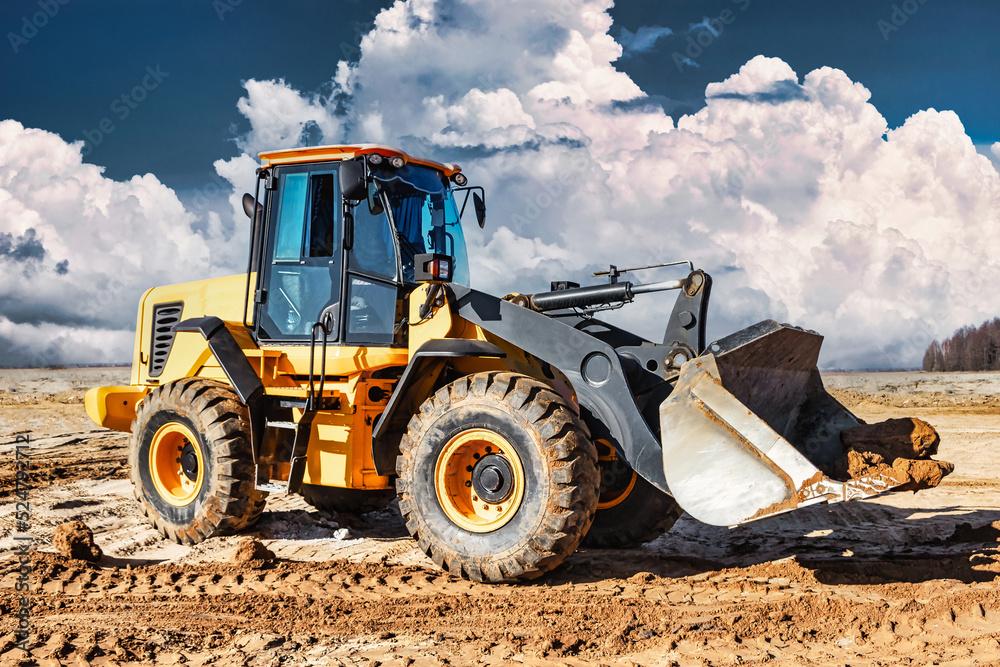 Wall mural Powerful bulldozer or loader moves the earth at the construction site against the sky. An earthmoving machine is leveling the site. Construction heavy equipment for earthworks.