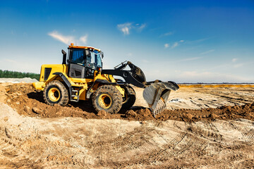 Powerful bulldozer or loader moves the earth at the construction site against the sky. An earthmoving machine is leveling the site. Construction heavy equipment for earthworks.