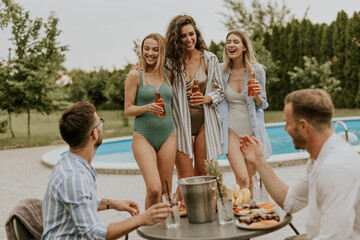 Group of young people cheering with drinks and eating fruits by the pool in the garden