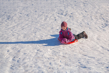 Fototapeta na wymiar Happy girl sliding down the hill on saucer sled. Girl enyoing slider ride on the snow