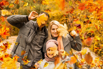 family, childhood, season and people concept - happy family playing with autumn leaves in park