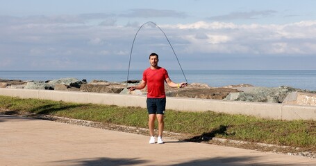 Caucasian athletic sportsman working out with jumping rope on nature.