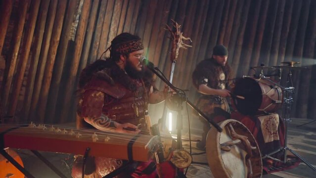 Frontman of folk rock band plays bow instrument singing by throat on stage in ail. Shamanic rituals and music show. Siberian meditative sound