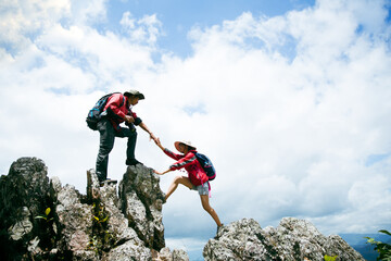 Person hike friends helping each other up a mountain. Man and woman giving a helping hand and...