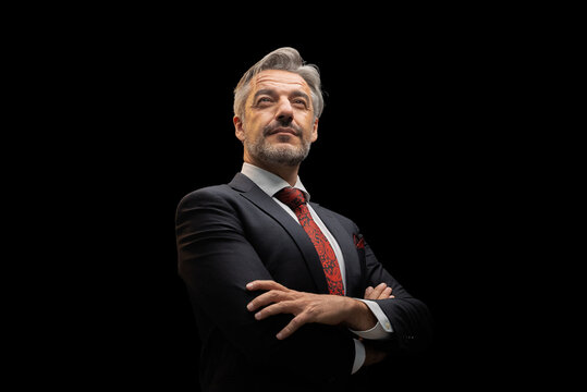 Portrait of senior Businessman standing in elegant black suit and red tie with arms crossed. isolated on black background.