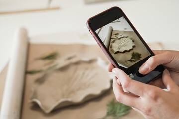 Taking picture of handmade ceramics on workshop. Pottery blog owner making photo of clay plate on...
