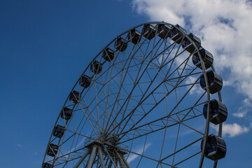Fototapeta na wymiar Large metal Ferris wheel close-up against a blue sky with white clouds in Vladimir russia