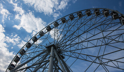 Vladimir, Russia - August, 16, 2022: Large metal Ferris wheel close-up against a blue sky with white clouds in town central park