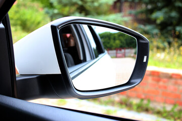 Side rear-view mirror on a modern car. Rear view mirror with beautiful reflection. Close up rearview mirror lux car on the background of green trees.