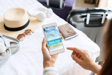 Woman hand holding smartphone with travel accessories on bed in hotel room. Travel, relaxation,...