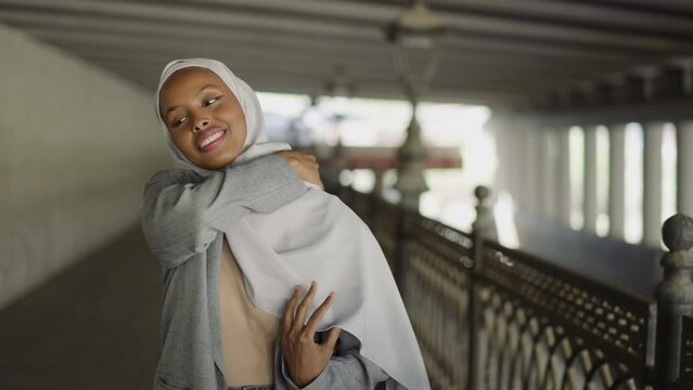 Smiling black woman wraps shoulder with hijab on waterfront